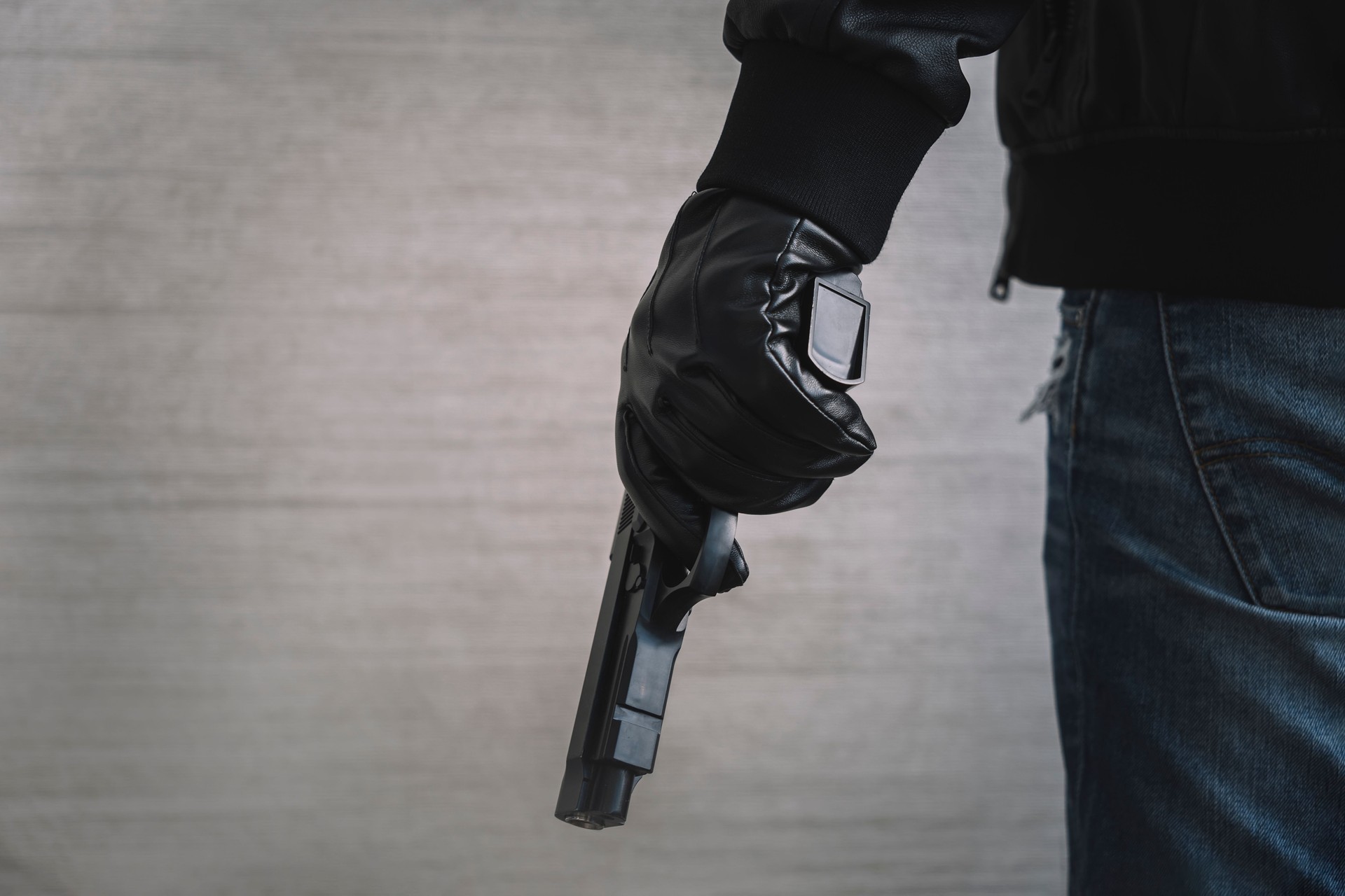 The concept of the crime of banditry. A dangerous shooter and a black pistol on a dark background. hired killer is preparing to shoot. Pulls a firearm out of his jacket pocket